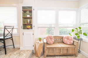 White built-in cabinetry with glass display shelves, wood-finish flooring, and multiple large windows featuring window blinds