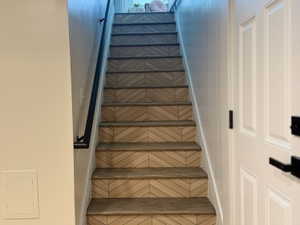 Staircase featuring chevron pattern risers and wood treads, complemented by a black handrail and white wainscoting