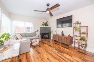 Spacious living area featuring hardwood flooring, a ceiling fan, and a fireplace with a decorative mantel
