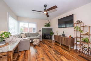 Living space featuring hardwood flooring, corner electric fireplace with a dark shiplap accent, and a ceiling fan with integrated lighting