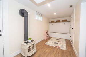 Room featuring a freestanding stove with an exposed flue, wood-finish flooring, recessed lighting, and a built-in bench with coat hooks and shelving