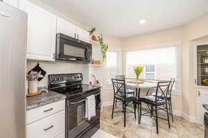 Kitchen featuring white cabinetry, dark stone-finish countertops, and black appliances