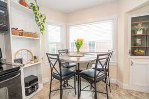 Dining area featuring a round stone-finish table with seating for four, two large windows with blinds, built-in shelving, and tile flooring