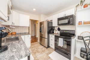 Kitchen featuring white cabinetry, textured countertops, stainless steel appliances, including a side-by-side refrigerator, tile flooring, and a recessed smart ceiling light