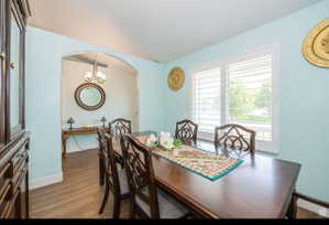 Dining area featuring wood-finish flooring, a large window with white plantation shutters, and an arched entryway
