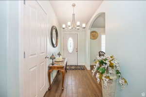 Inviting entry featuring wood-finish flooring, a contemporary chandelier, arched doorway, and a white front door with decorative glass inlay
