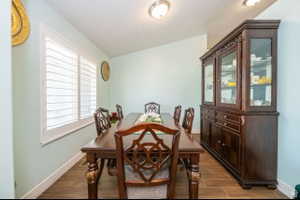 Spacious dining area featuring wood-finish tile flooring, a large window with white plantation shutters, and a built-in display cabinet with glass doors