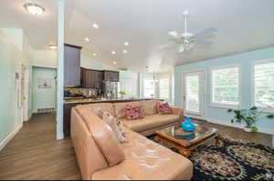 Open-concept living area featuring vaulted ceilings, wood-finish flooring, a ceiling fan, and multiple windows with white plantation shutters
