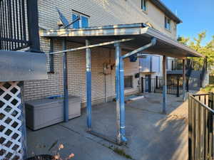 Covered concrete patio with a brick exterior, featuring an overhead structure and exterior lighting