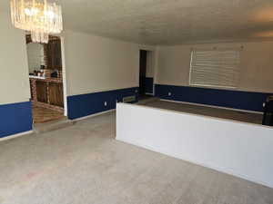 Expansive carpeted area featuring a partial wall partition, a crystal-style chandelier, and a stepped entry