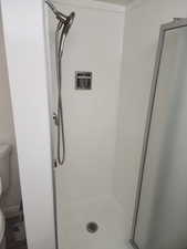 Walk-in shower with white tiled walls, brushed nickel showerhead and handheld sprayer, recessed storage niche, and a frosted glass enclosure