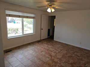 Spacious room featuring neutral wall tones, large window with blinds, tile flooring, and a ceiling fan with integrated lighting