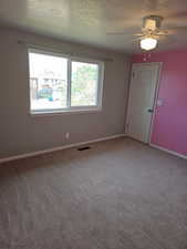 Room featuring soft gray carpeting, a multi-pane window with white trim, a solid white door, and a ceiling fan with integrated lighting