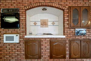 Brick wall featuring an arched alcove with white tile backsplash, an inset cooktop, and a solid surface countertop