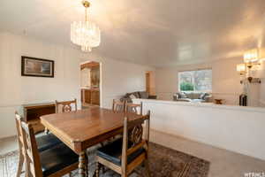 Dining area featuring a crystal chandelier, neutral wall paint, and a low partial wall opening to a living room with a large window