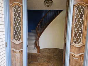 Entry foyer featuring a curved staircase with wood banister, stone tile flooring, and an ornate ceiling fixture
