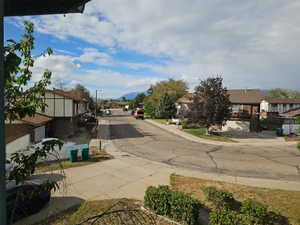 Residential streetscape featuring a paved roadway with curb-lined sidewalks and mature trees