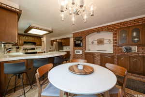 Kitchen and dining area featuring a light fixture, tile flooring, brick wall detailing, built-in cabinetry, and a curved breakfast bar with a tile countertop