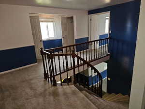 Upper-level landing featuring a wood-finish staircase railing, carpeted flooring, and a window with blinds