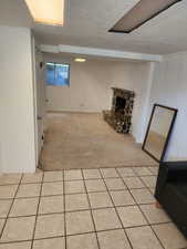 Spacious room featuring a stone fireplace, light-toned carpeting, and a window with security bars
