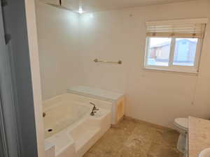 Bathroom featuring a built-in white bathtub, tiled flooring, a window with blinds, and a toilet