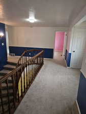 Carpeted upper landing featuring a wood banister, white trim, and a flush-mount ceiling light