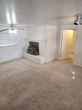 Living space featuring a whitewashed brick fireplace with a wood-burning stove insert, track lighting, and a ceiling fan