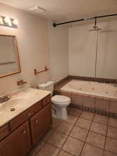 Full bathroom featuring a single vanity with wood-finish cabinetry, a built-in jetted tub with tile surround, a standard toilet, and tiled flooring