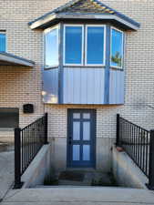 Light-colored brick exterior featuring a bay window with a shingled roofline and a lower-level entry with a blue paneled door
