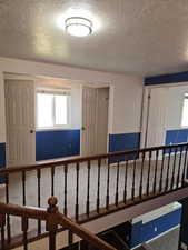 Upper-level landing featuring wood banister, neutral carpeting, and a flush-mount ceiling light