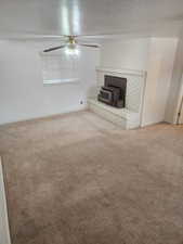 Living space featuring a brick fireplace with an integrated wood-burning stove, a ceiling fan, and carpeted flooring