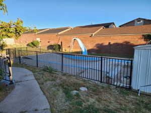 Private backyard featuring a fenced-in swimming pool with a slide, a concrete pathway, and mature trees