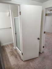 Bathroom entry featuring a glass-enclosed shower with a frosted panel and wood-finish flooring