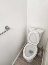 White ceramic toilet with a matching tank and seat, wood-finish flooring, white baseboards, and a wall-mounted metal towel bar