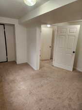 Carpeted room featuring white walls and trim, overhead lighting, and multiple white doors with black hardware