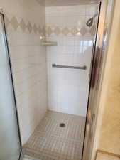 Tiled shower stall featuring a chrome shower head, a built-in soap dish, a grab bar, and a patterned accent tile band