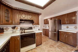 Kitchen featuring wood cabinetry, white tiled countertops, and a tiled backsplash with decorative accents