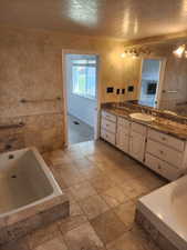 Bathroom featuring a built-in soaking tub, tile flooring, and a double vanity with a stone countertop