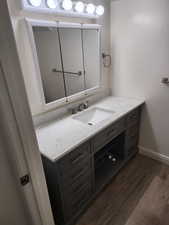 Bathroom vanity featuring a quartz-finish countertop with an integrated sink, a brushed nickel faucet, a medicine cabinet with mirrored doors, a vanity light fixture, and wood-finish flooring