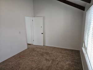 Carpeted room featuring a vaulted ceiling with exposed wood beams, white walls, and a window with blinds