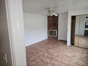 Interior room featuring tiled flooring, a brick fireplace, ceiling fan, and mirrored closet doors