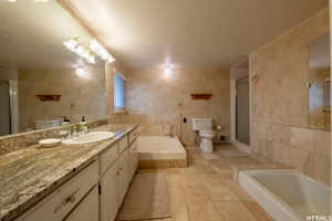 Bathroom featuring a dual vanity with a patterned countertop and white cabinetry, a built-in soaking tub, a stand-up shower, and tiled flooring