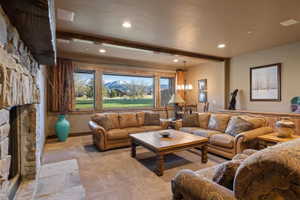 Carpeted living room featuring beam ceiling, a fireplace, and a chandelier