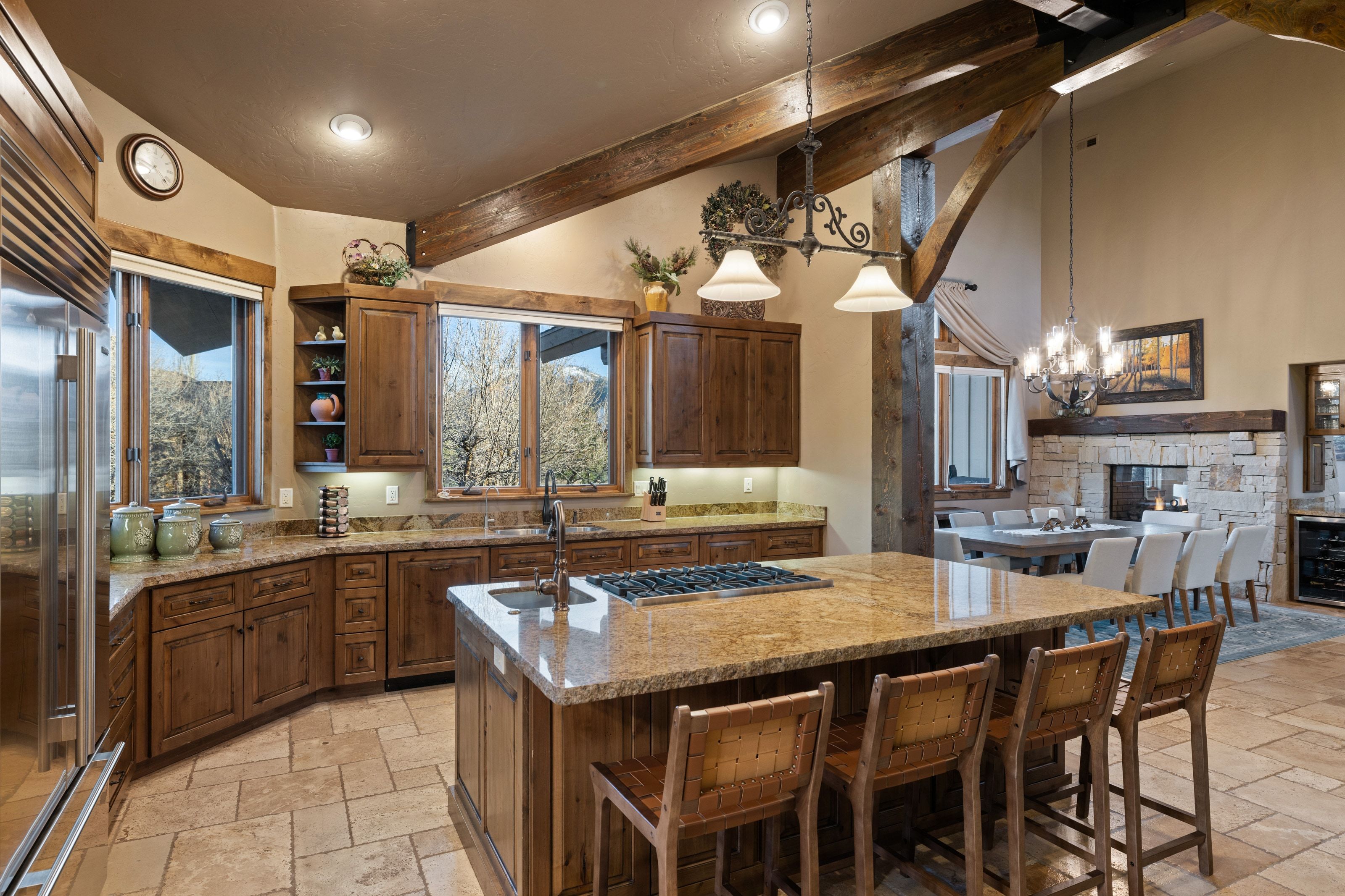 Kitchen featuring stone tile floors, lofted ceiling, a center island with sink, and light stone countertops