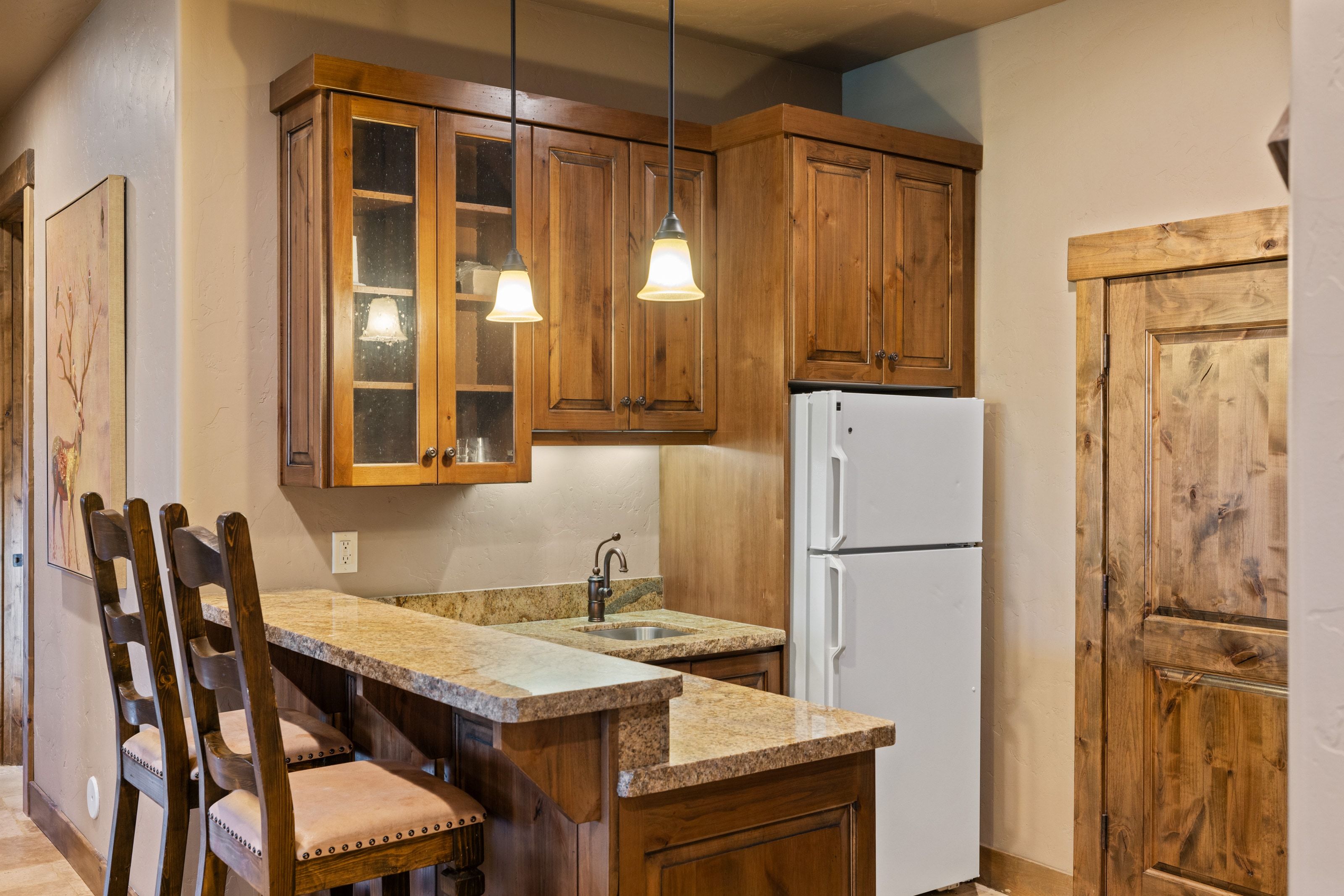 Kitchen with freestanding refrigerator, hanging light fixtures, glass fronted cabinets, a peninsula, and wood finish cabinetry