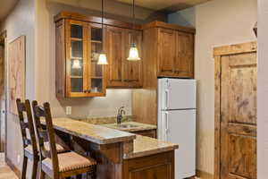 Kitchen with freestanding refrigerator, hanging light fixtures, glass fronted cabinets, a peninsula, and wood finish cabinetry