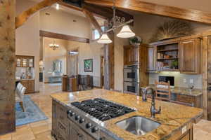 Kitchen with stone tile floors, stainless steel appliances, light stone counters, open shelves, and lofted ceiling
