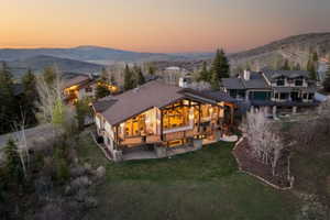 Back of house with a deck with mountain view, roof with shingles, a lawn, and a chimney