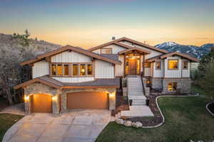 View of front of house with stone siding, a garage, driveway, a lawn, and a mountain view
