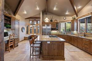 Kitchen featuring open shelves, stone tile floors, hanging light fixtures, a kitchen island with sink, and lofted ceiling